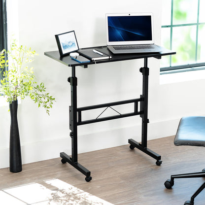 Adjustable standing desk with laptop on a wooden floor near a window.