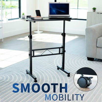Adjustable standing desk with laptop on a carpeted floor in a room with a couch and windows.