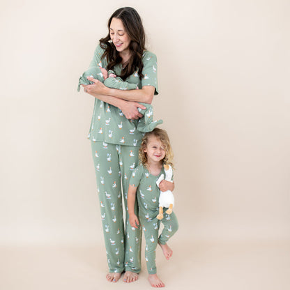 Family matching in Silly Goose. Mother wearing the Women's V-Neck and Lounge pants holding her newborn in a take me home set with Cap with her oldest child standing beside her wearing the short sleeve toddler pajamas with pant holding a toy stuffed goose