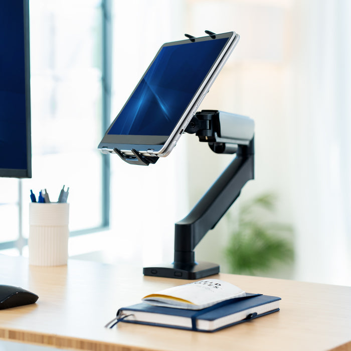 Tablet on a stand on a desk with a notebook and pens in the background