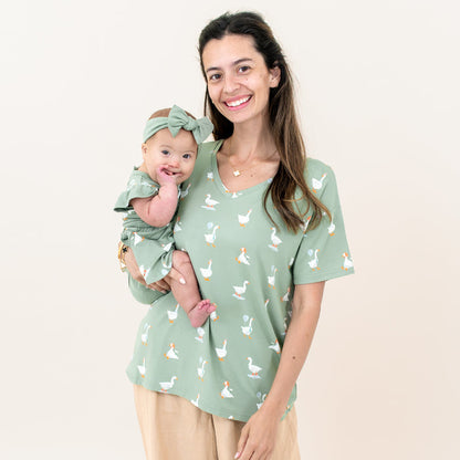 Mother wearing the Silly Goose Women's V-Neck holding her infant daughter who is matching in a Twirl Bodysuit Dress in Silly Goose and knotted bow headband in Thyme