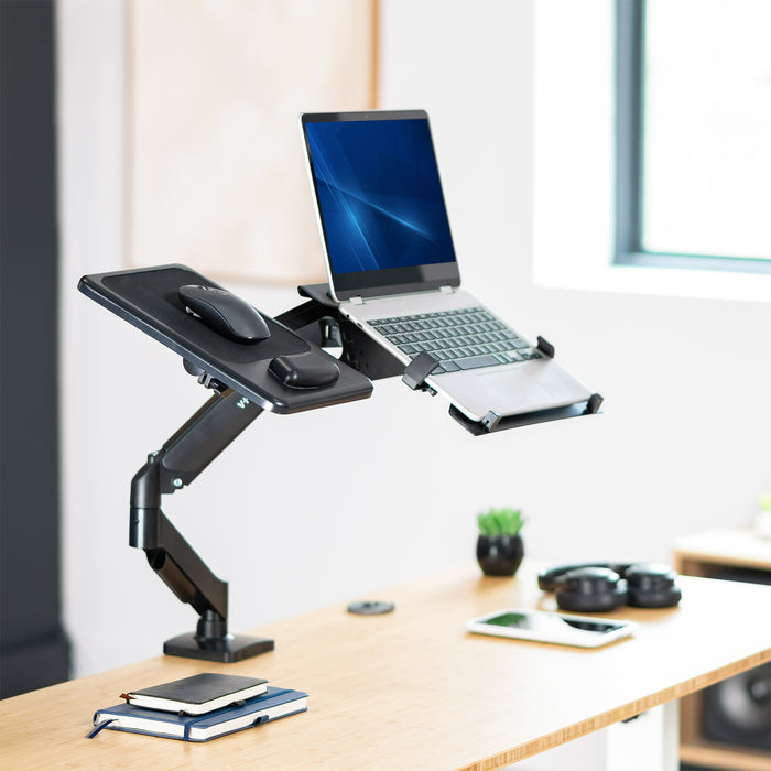 Adjustable desk stand with laptop, mouse, and phone on a wooden desk.