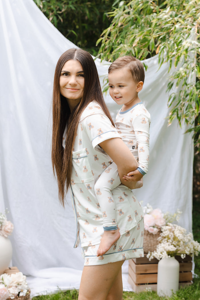 Mom holding toddler on her back outdoors wearing matching teddy bear patterned pajamas